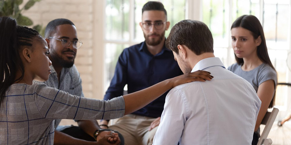 A woman comforts the man next to her in a group therapy session.