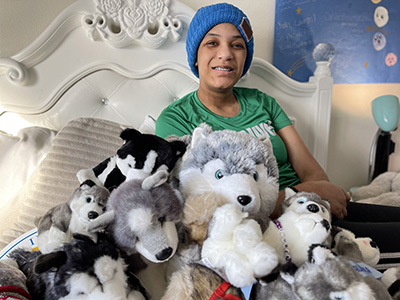 Lauren on bed with a dozen stuffed animals shaped like Huskies